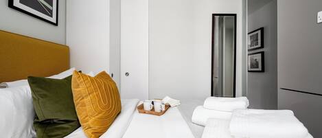 Une chambre d’hôtel avec un lit, une table de chevet sur laquelle se trouve une assiette avec des tasses blanches et un livre, et une armoire.