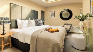 Ett hotellrum med en säng, ett skrivbord, en stol, ett glasbord, en rund spegel och en vas med blommor.