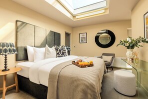 A hotel room with a bed, a desk, a chair, a glass table, a round mirror, and a vase with flowers. - Liverpool Street - Your Apartment (London)