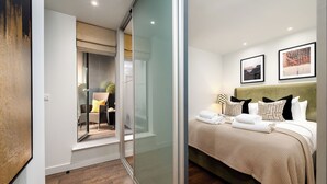 Ett modernt hotellrum med en glasvägg, en säng med prydligt hopvikta handdukar och två inramade tavlor på väggen.