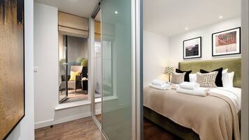 A modern hotel room with a glass partition, a bed with neatly folded towels, and two framed pictures on the wall.