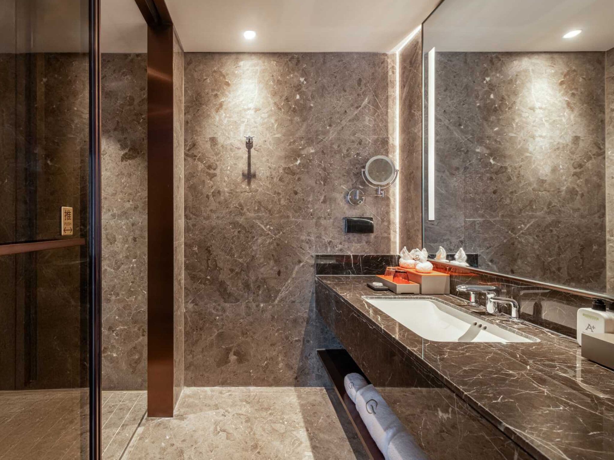 Un bagno moderno con un grande specchio, pareti in marmo e un lavello a incasso.