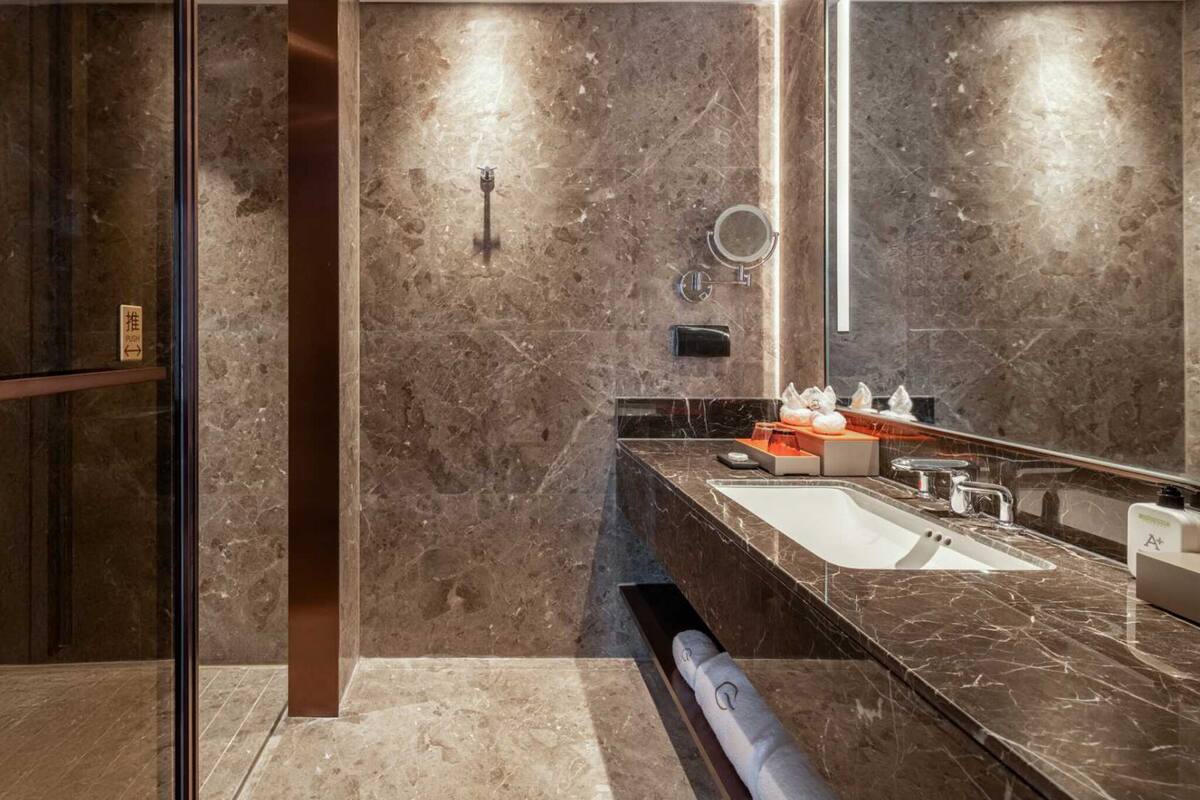 Un bagno moderno con un grande specchio, pareti in marmo e un lavello a incasso.