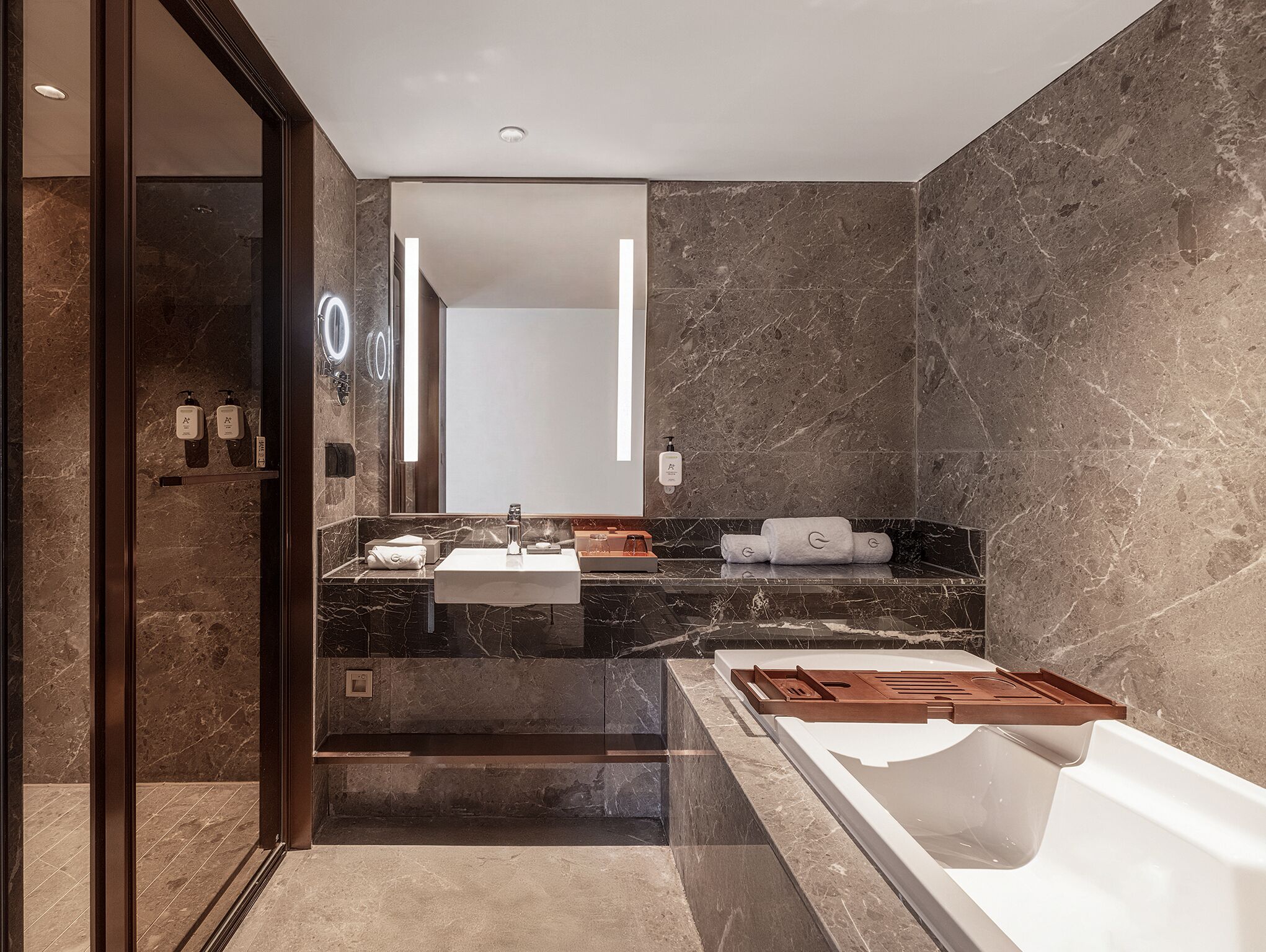 Un bagno moderno con un grande specchio, due lavabi, una vasca e pareti in marmo.