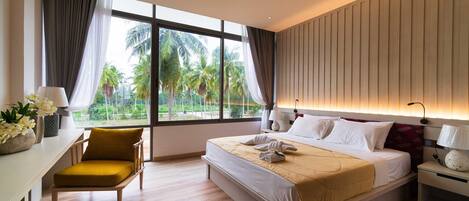 A modern hotel room with a large bed, a desk with a chair, and a view of palm trees through large windows.