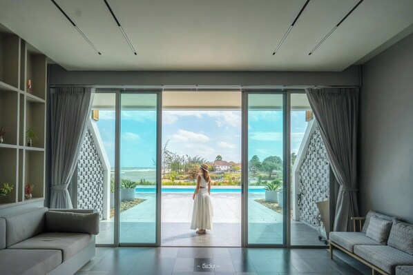 A modern interior with a large sliding glass door leading to a pool area, a sofa, and a bookshelf.