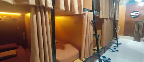A bunk bed room with curtains, a bed, and a sign for 'Capsotel'.
