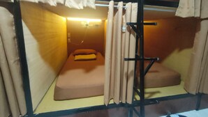 A small, compact room with a single bed, a small table, and a curtain. - Capsutel (Baguio)