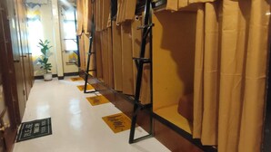 A hotel corridor with a row of rooms, each with a door and a window. There are yellow signs on the floor indicating the rooms. - Capsutel (Baguio)