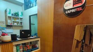 A hotel reception desk with a computer, a mirror, and a sign that reads 'CAPSULE.' - Capsutel (Baguio)