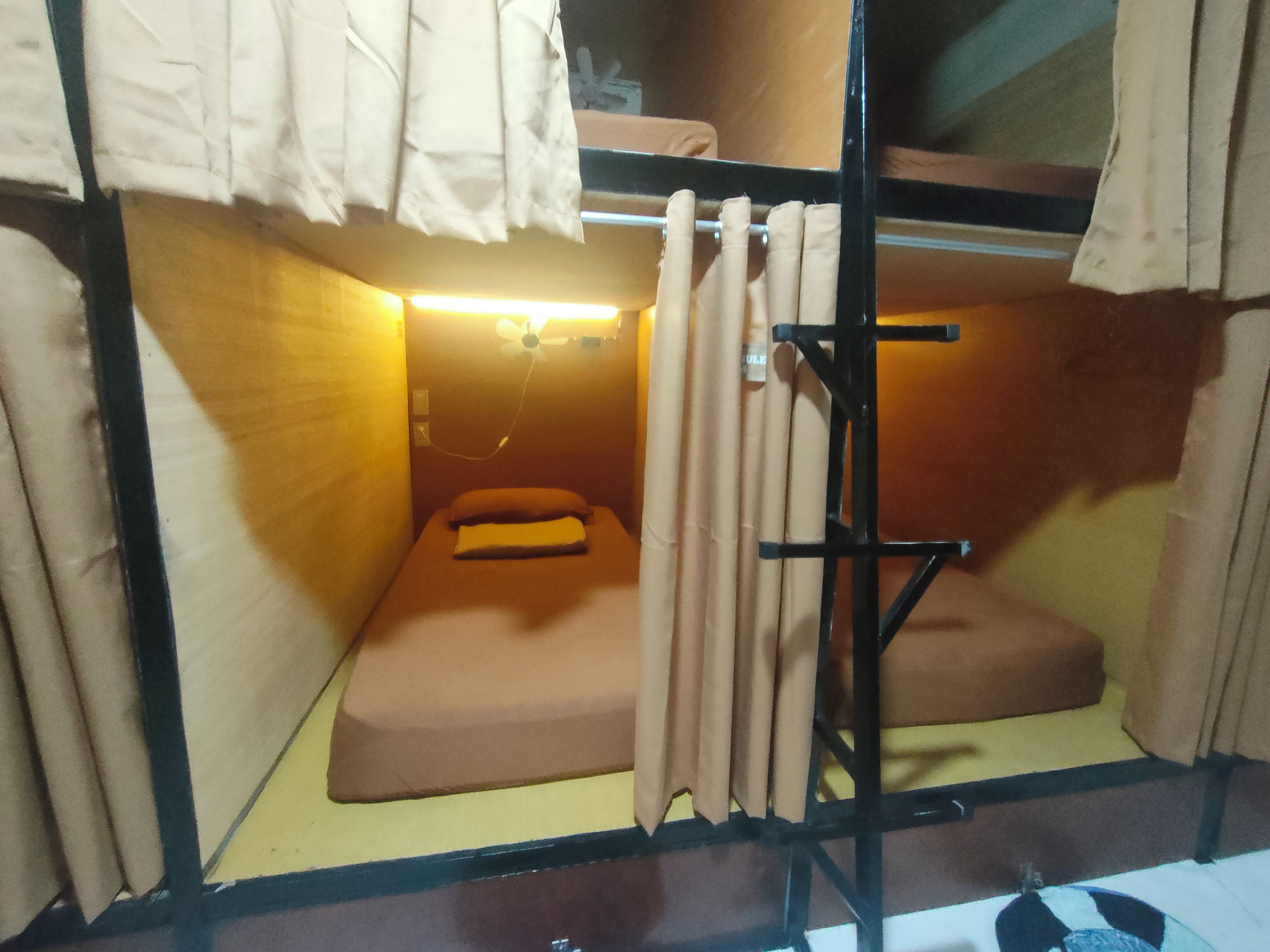 Una habitación pequeña y funcional con una cama individual, una mesita y una cortina.