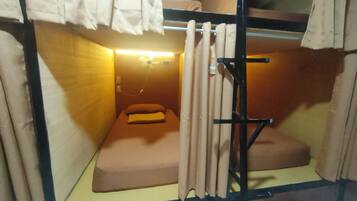 Una habitación pequeña y funcional con una cama individual, una mesita y una cortina.