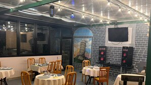 A restaurant with round tables and chairs, a brick wall, a TV mounted on the wall, and a ceiling with exposed pipes and lights. - Papillat Vip Llc (Batumi)