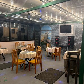 A restaurant with round tables and chairs, a brick wall, a TV mounted on the wall, and a ceiling with exposed pipes and lights. - Papillat Vip Llc (Batumi)