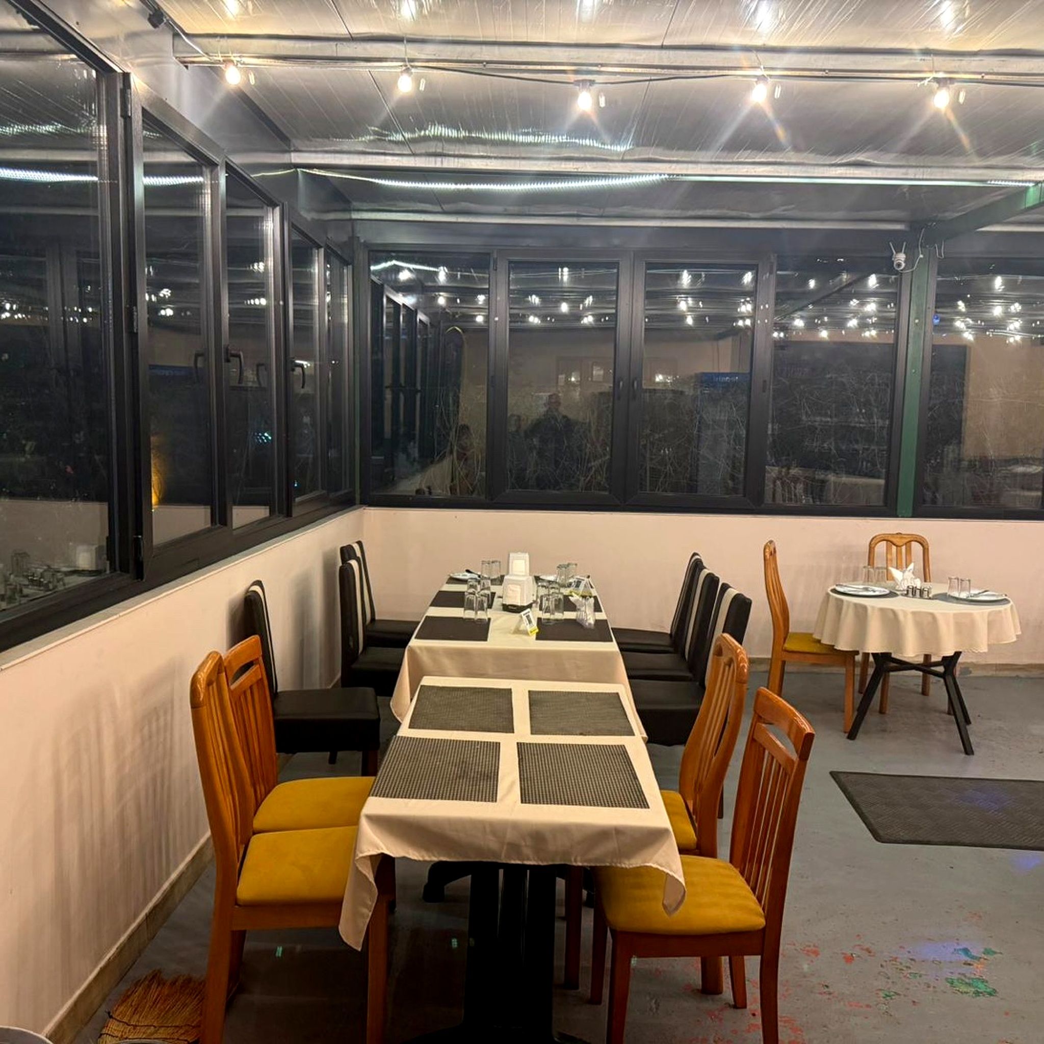 A dining area with a long table set for four, surrounded by chairs with yellow cushions.