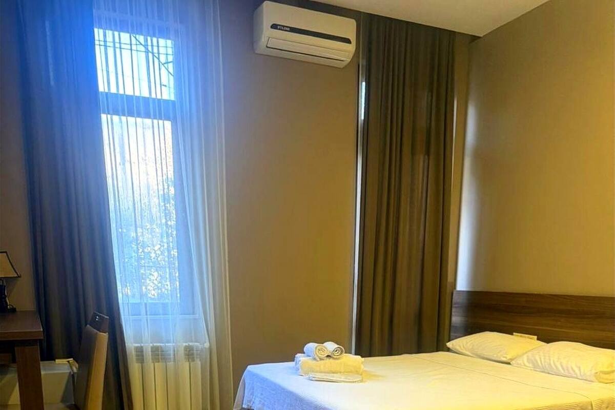 A hotel room with a bed, a chair, a desk, and an air conditioning unit.