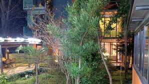 Une cour avec un petit arbre, une clôture et un bâtiment doté de grandes fenêtres.