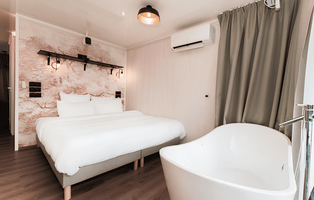A bedroom with a bed, a large white bathtub, and a wall-mounted air conditioning unit.