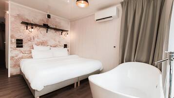 A bedroom with a bed, a large white bathtub, and a wall-mounted air conditioning unit.
