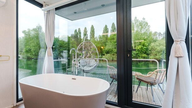 A modern bathroom with a freestanding bathtub, a glass-enclosed shower, and a view of a wooden deck and greenery outside. - Royale Escale Torcy (Torcy)