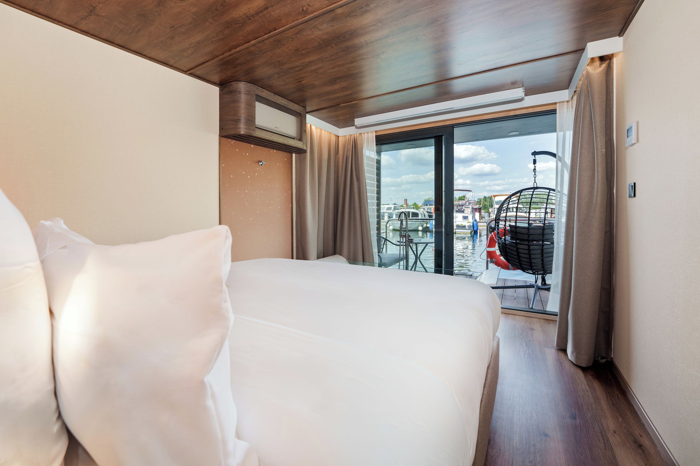 A hotel room with a large bed, a view of the outside, and a balcony with a chair and a hanging chair.