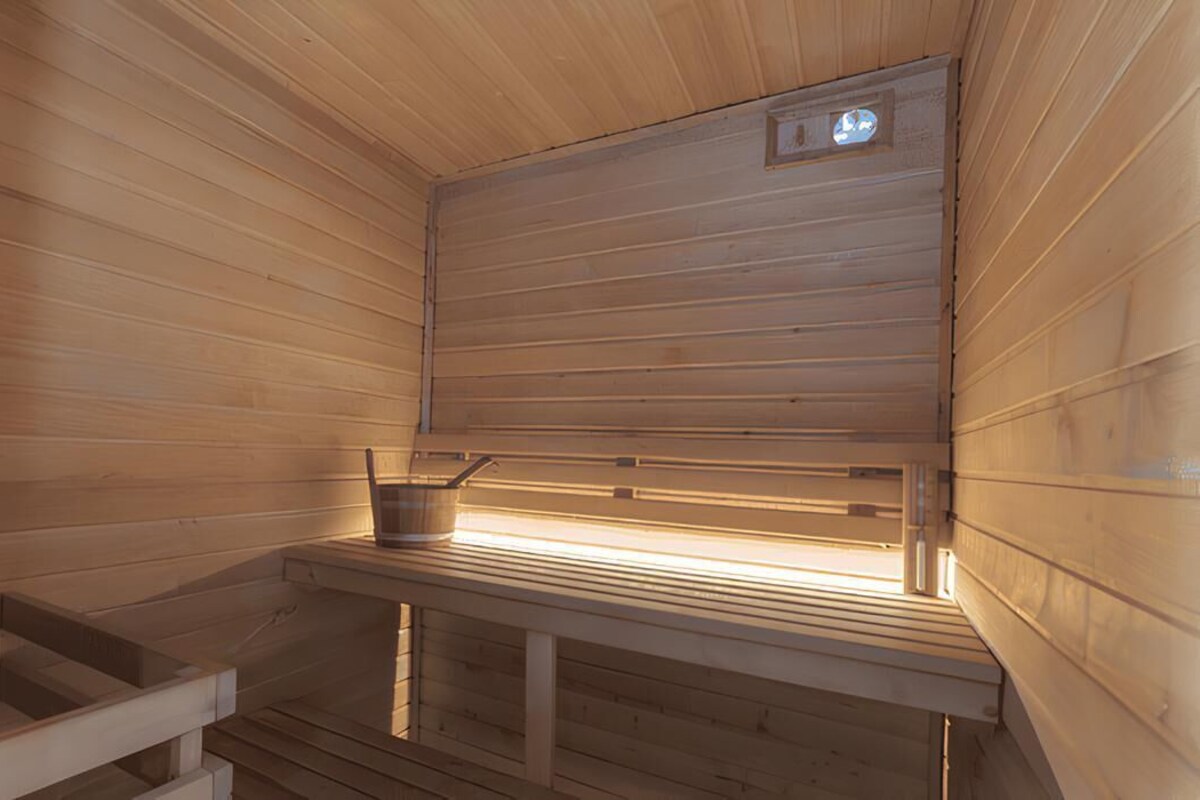 A sauna with wooden walls and benches, a visible heating element, and a small window with a light.