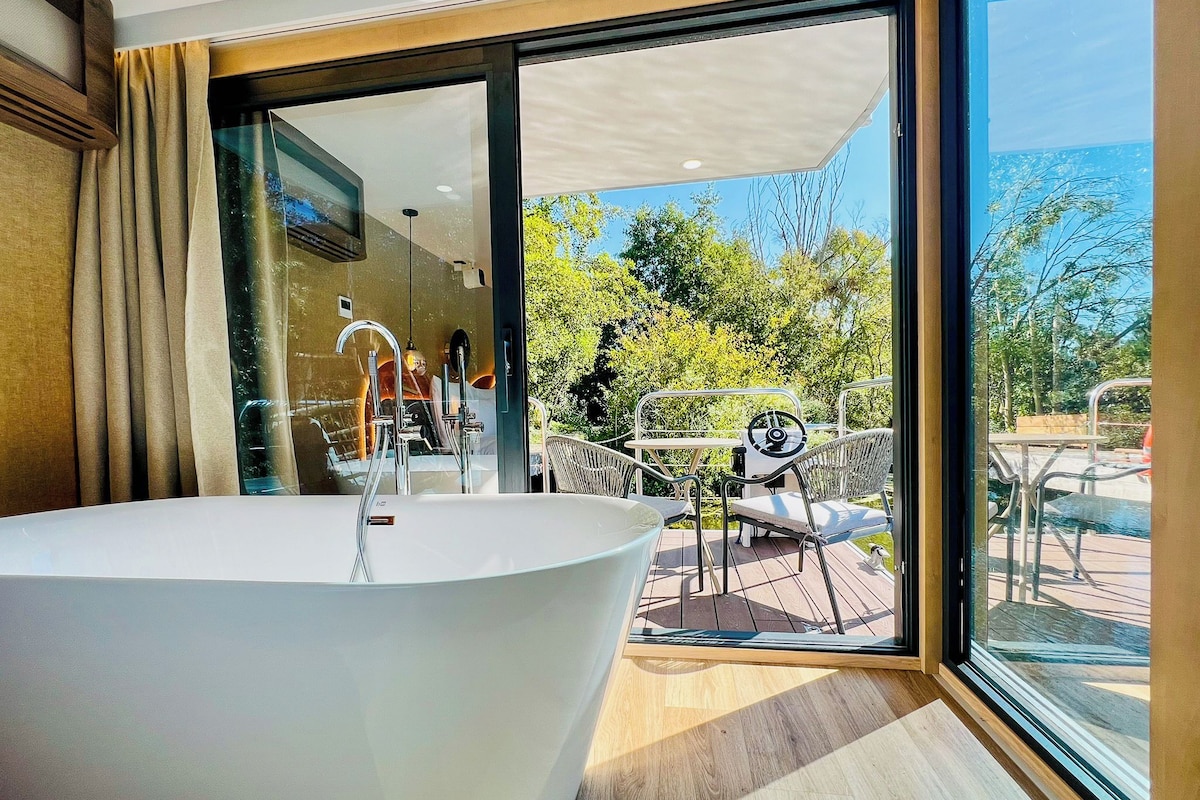 A modern bathroom with a freestanding bathtub, a glass shower enclosure, and a view of an outdoor deck with outdoor furniture.