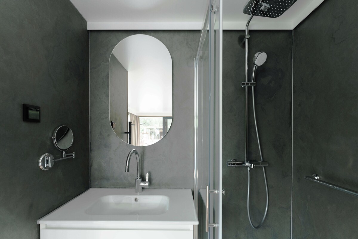 A modern bathroom with a white sink, a round mirror, and a shower with a handheld showerhead.