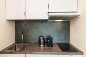 A compact kitchen with a stainless steel sink, a kettle, and a portable induction cooktop.