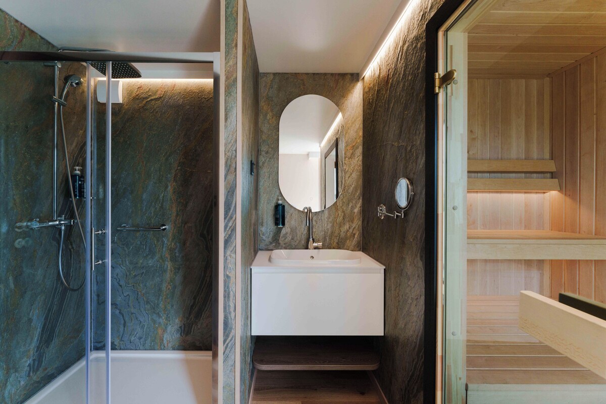 A modern bathroom with a glass-enclosed shower, a white sink with a mirror, and wooden paneling on the walls.