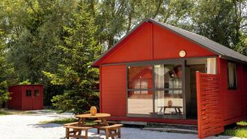 A red cabin with a large window, a wooden table, and a bench outside.