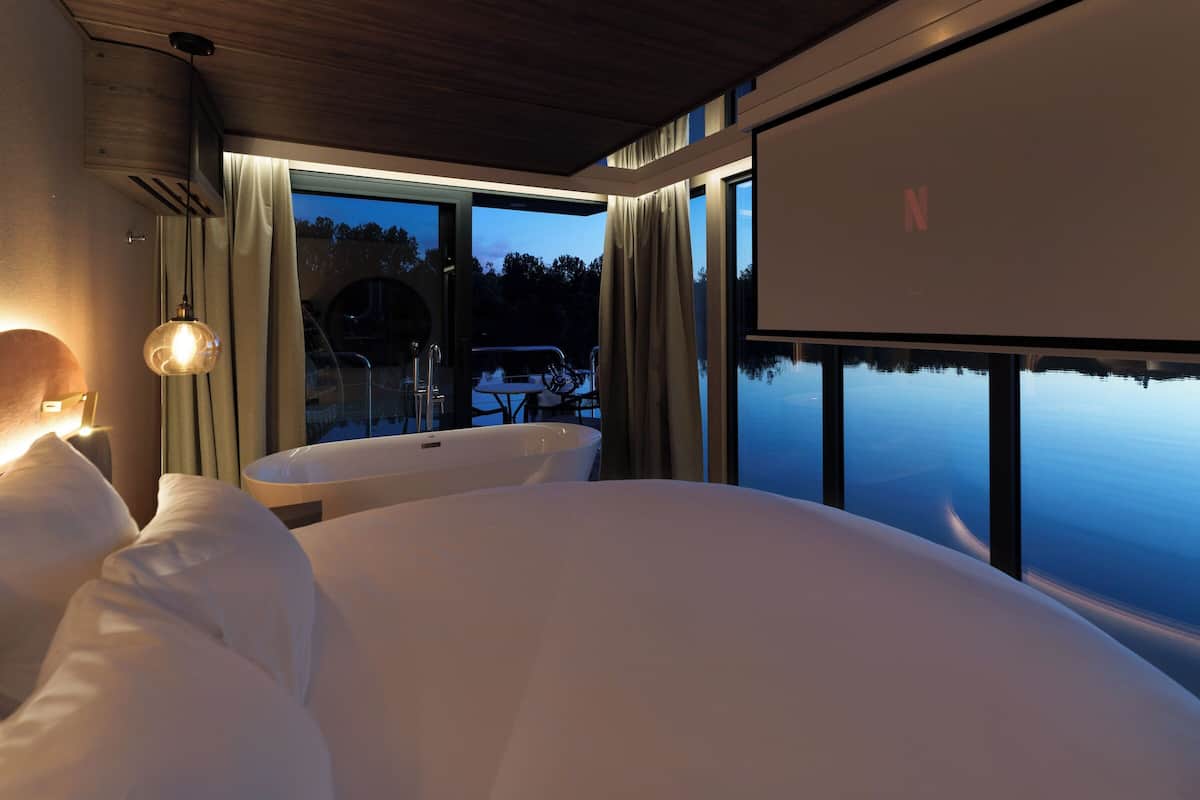 Un dormitorio moderno con una cama grande, una bañera y vista a un cuerpo de agua.