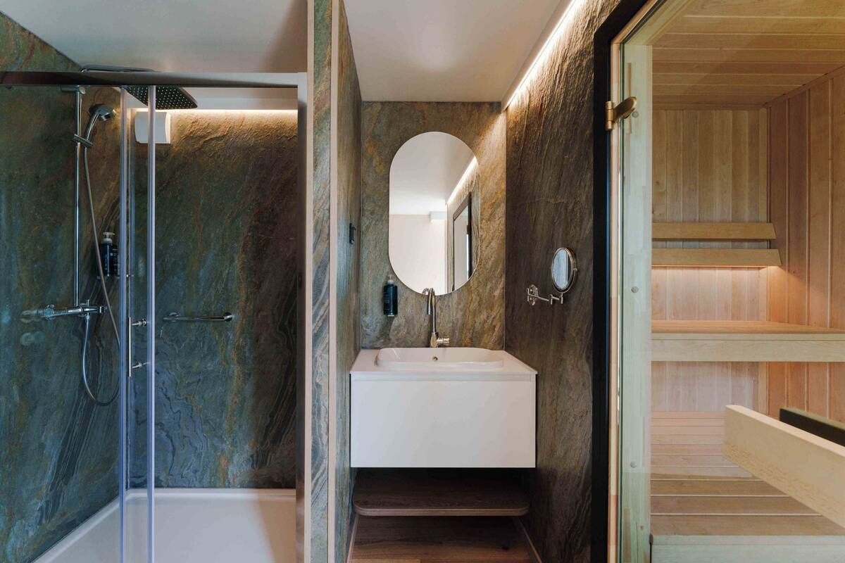Un baño moderno con ducha envuelta en vidrio, un lavamanos blanco con espejo y paneles de madera en las paredes.