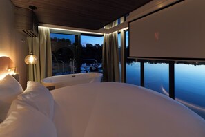 A modern bedroom with a large bed, a bathtub, and a view of a body of water. - Royale Escale Torcy (Torcy)