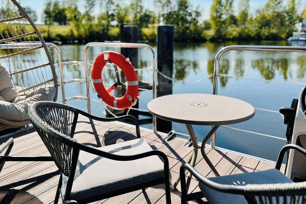 A deck with a table and chairs, a life preserver, and a calm water body in the background.