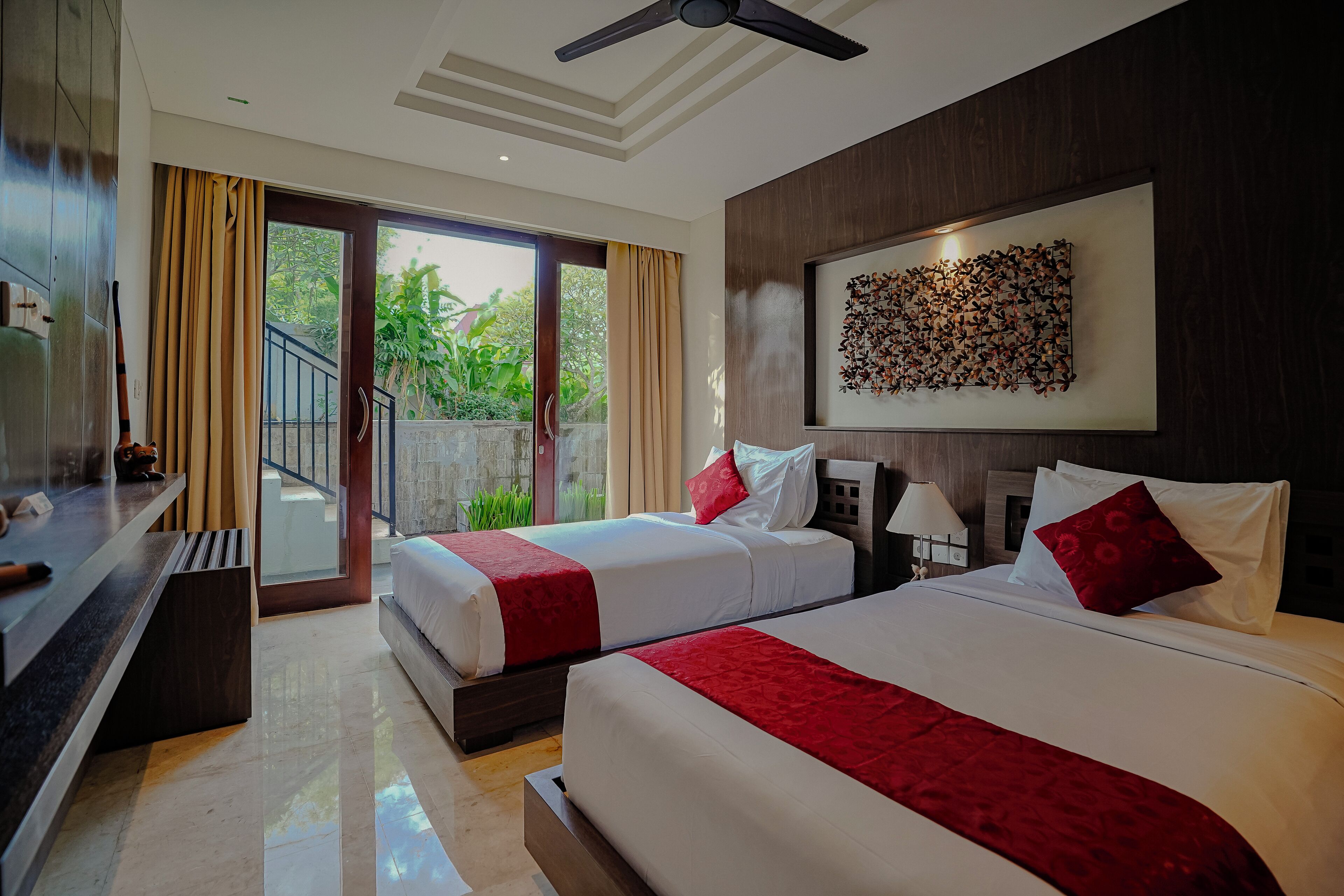 A hotel room with two beds, a balcony, a ceiling fan, and a wall-mounted artwork.