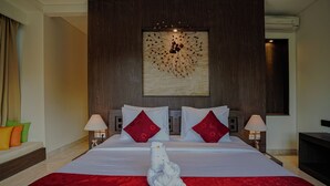 A hotel room with a large bed, two red pillows, a white towel sculpture, and a wall art piece. - Campania Villa Bali (Sukawati)
