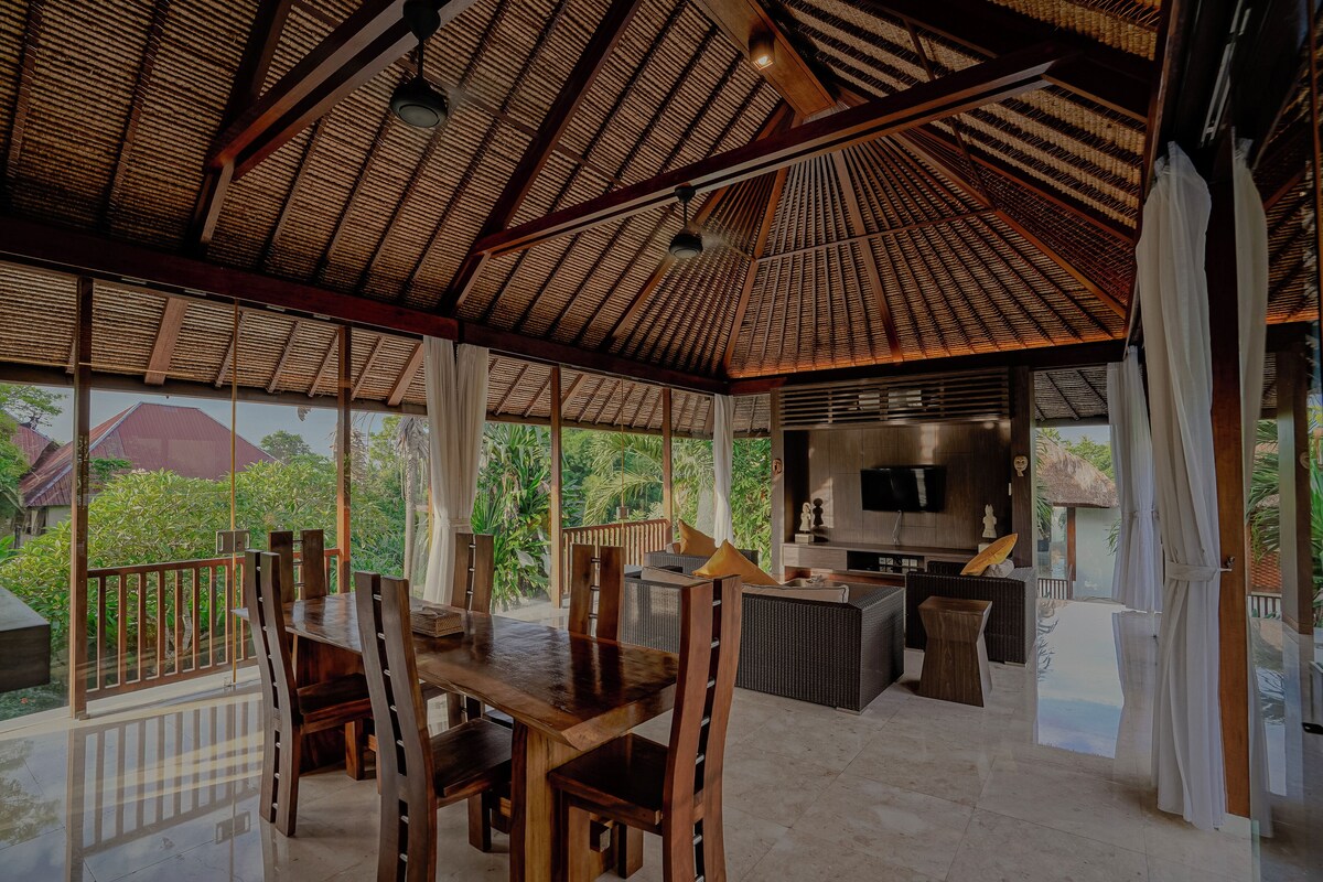 A spacious indoor area with a high ceiling, wooden furniture, and a large TV screen.
