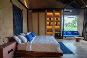 Ein Schlafzimmer mit Bett, Nachttisch und Blick auf ein blaues Sofa und Grünfläche draußen.