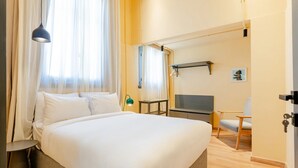 Una habitación de hotel con una cama, televisión, silla y escritorio.