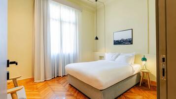 Un dormitorio ordenado con cama, mesita de noche, lámpara y ventana con cortinas.