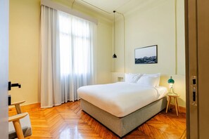 A neatly arranged bedroom with a bed, a nightstand, a lamp, and a window with curtains. - Studio Apartments Downtown Alexandria Menascehouse (Alexandria)