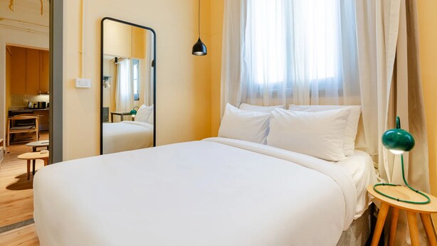 Une chambre d’hôtel avec un lit, un miroir, une lampe de chevet et une vue sur l’extérieur à travers des rideaux transparents.