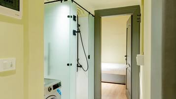 A compact hotel room with a washing machine, a shower area, and a bed.