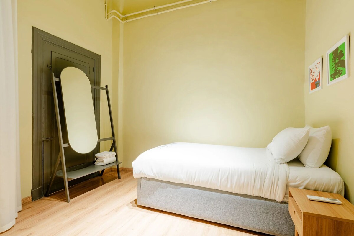 A bedroom with a bed, a wooden nightstand, a mirror, and a door.