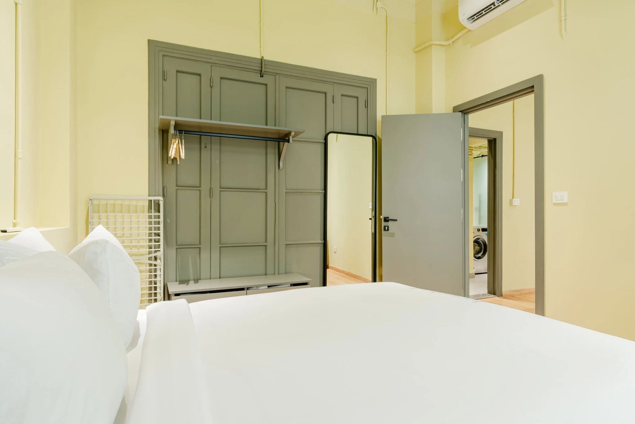 Una habitación de hotel con una cama, un armario, un espejo y una puerta que da a una zona de lavandería.