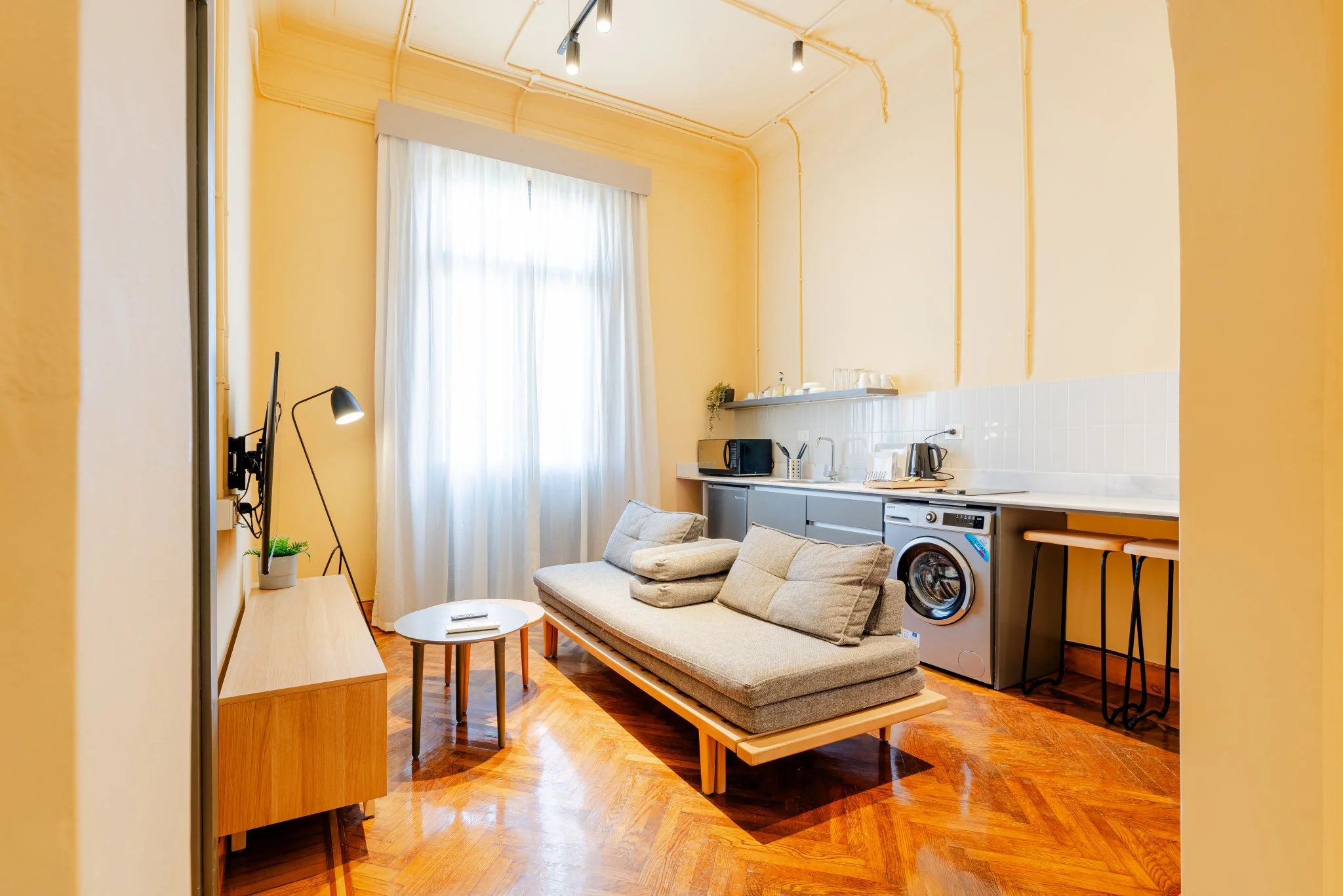 Un espacio habitable compacto con sofá, lavadora, mesita y lámpara.