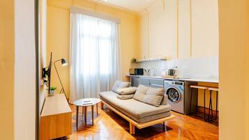 A compact living space with a sofa, a washing machine, a small table, and a lamp.