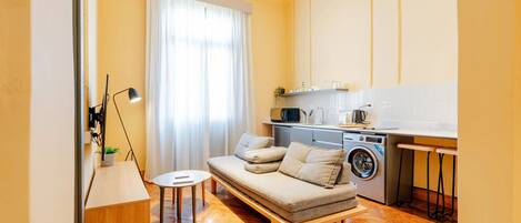 Un espacio habitable compacto con sofá, lavadora, mesita y lámpara.