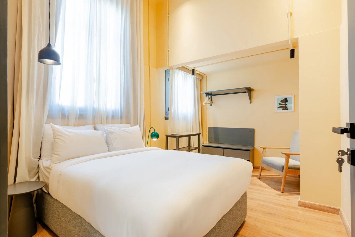 A hotel room with a bed, a TV, a chair, and a desk.